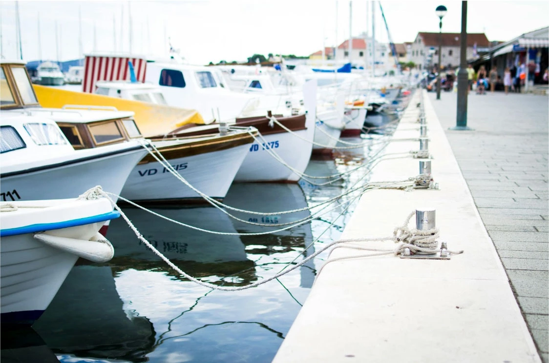 Small boats tied to a dock with ropes secured around a metal post at the harbour